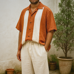 South Asian male model wearing rust orange and off-white two-tone oversized shirt with off-white linen drawstring pants in a minimal outdoor setting