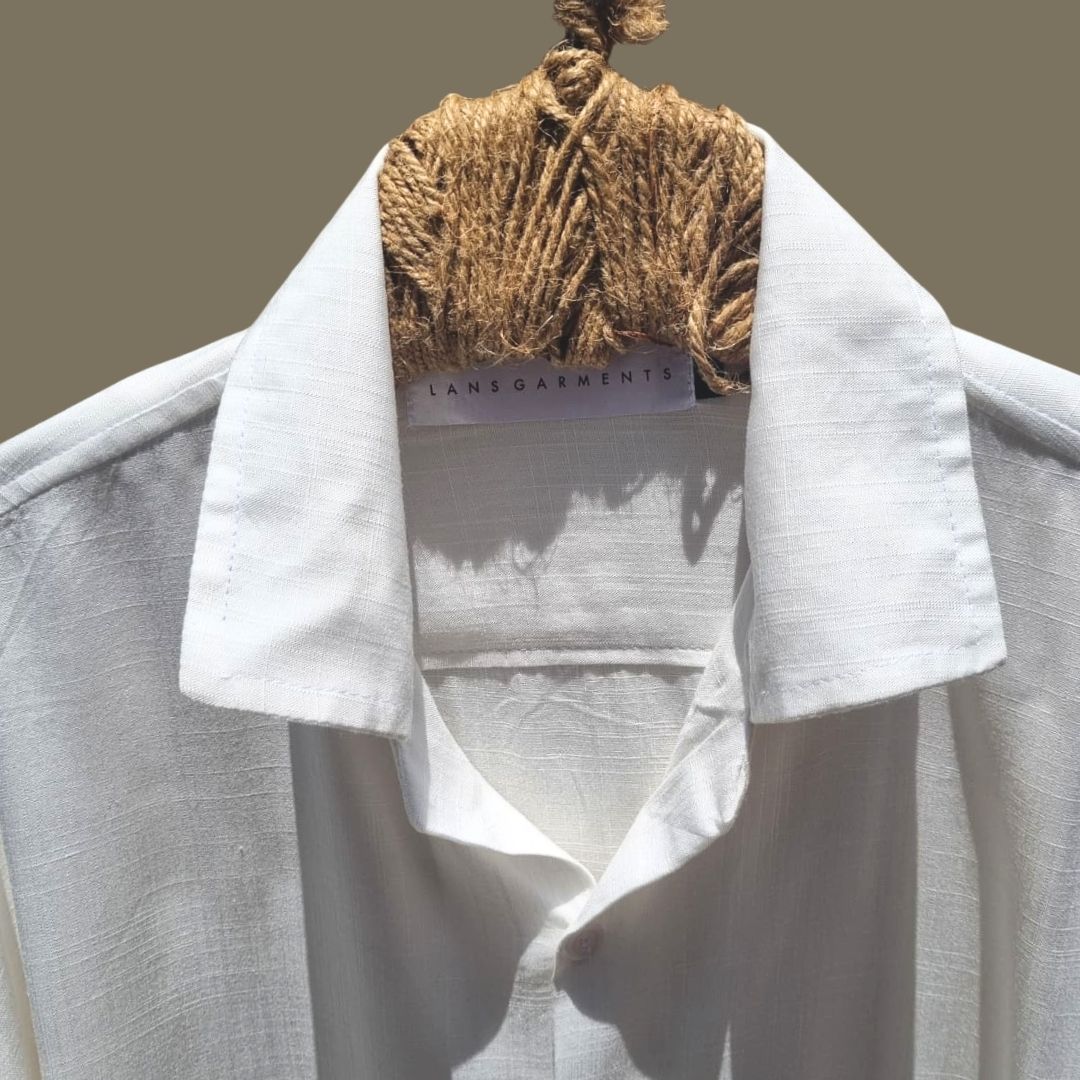 Relaxed Linen Shirt Collection – Black, Harvest Gold & Ivory | Lans Stack of three linen shirts in black, harvest gold, and ivory placed on a wooden stool — part of Lans’ Relaxed Cuban Collar Linen Collection.