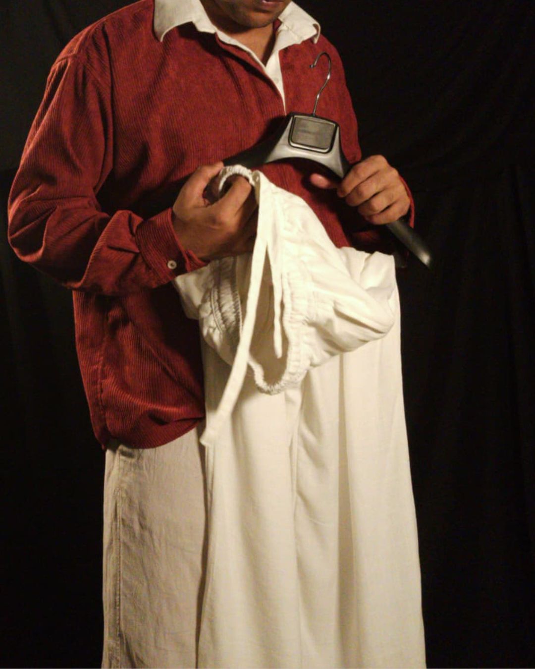 Generic male model wearing an oversized maroon corduroy retro long sleeve shirt with an off-white linen collar and oversized off-white linen drawstring pants on a plain studio background.