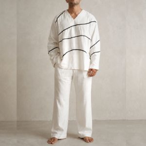 LANS Oversized Wave Runner white cotton V-neck shirt with black piping lines paired with oversized washed cotton pant in a light cement studio background.
