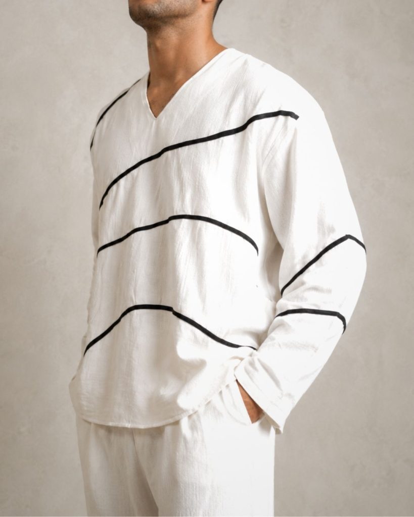 LANS Oversized Wave Runner white cotton V-neck shirt with black piping lines paired with oversized washed cotton pant in a light cement studio background.