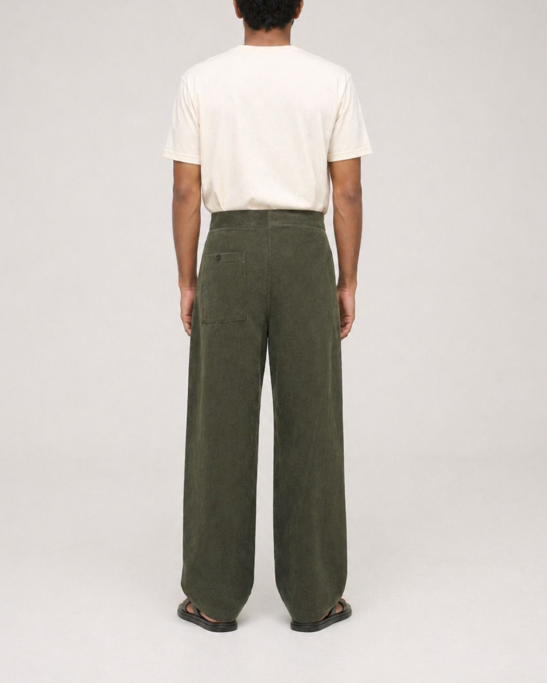 male model wearing dark olive green oversized corduroy Aldo pant with an off-white t-shirt on a plain studio background.